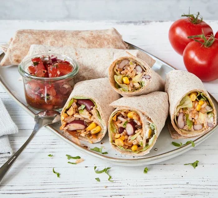 A white plate topped with a burrito next to a jar of salsa