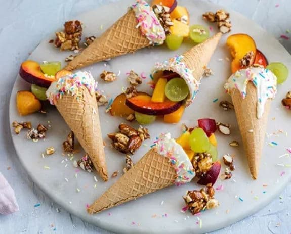 A white plate topped with three ice cream cones filled with fruit